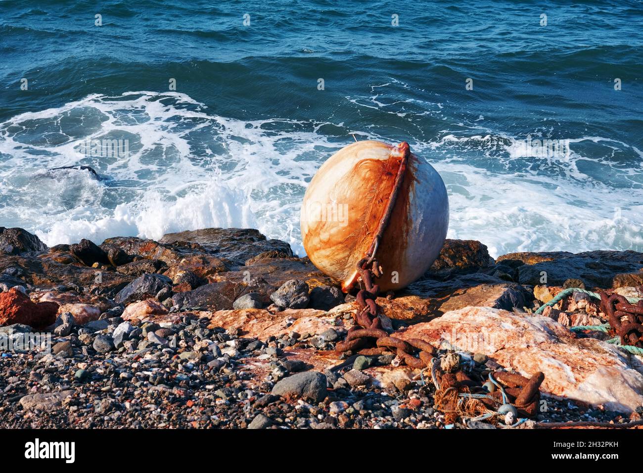 Big rusty white round buoy and chain on the shore with sea background. Stock Photo