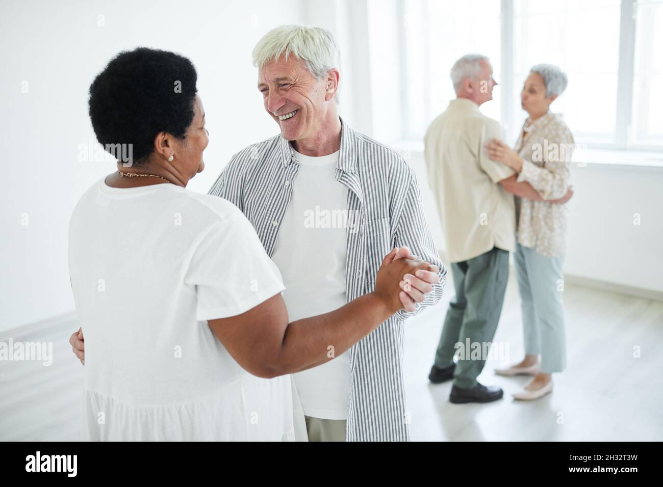 Two senior couples smiling to each other holding hands while dancing a slow dance in dance studio Stock Photo