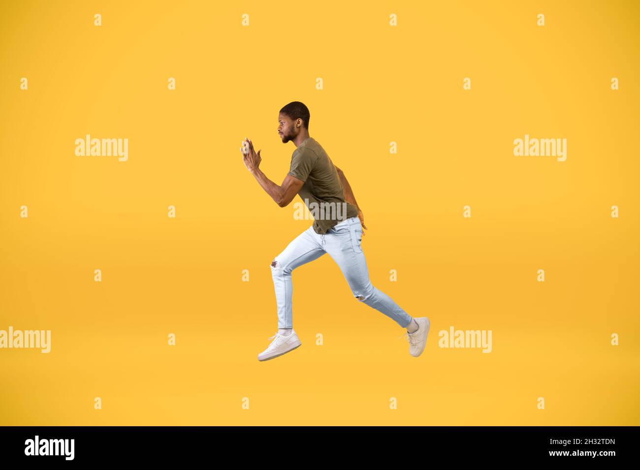 Young african american man running over yellow studio background, in motion side view shot of guy jumping in air, hurry up to sales or discounts Stock Photo