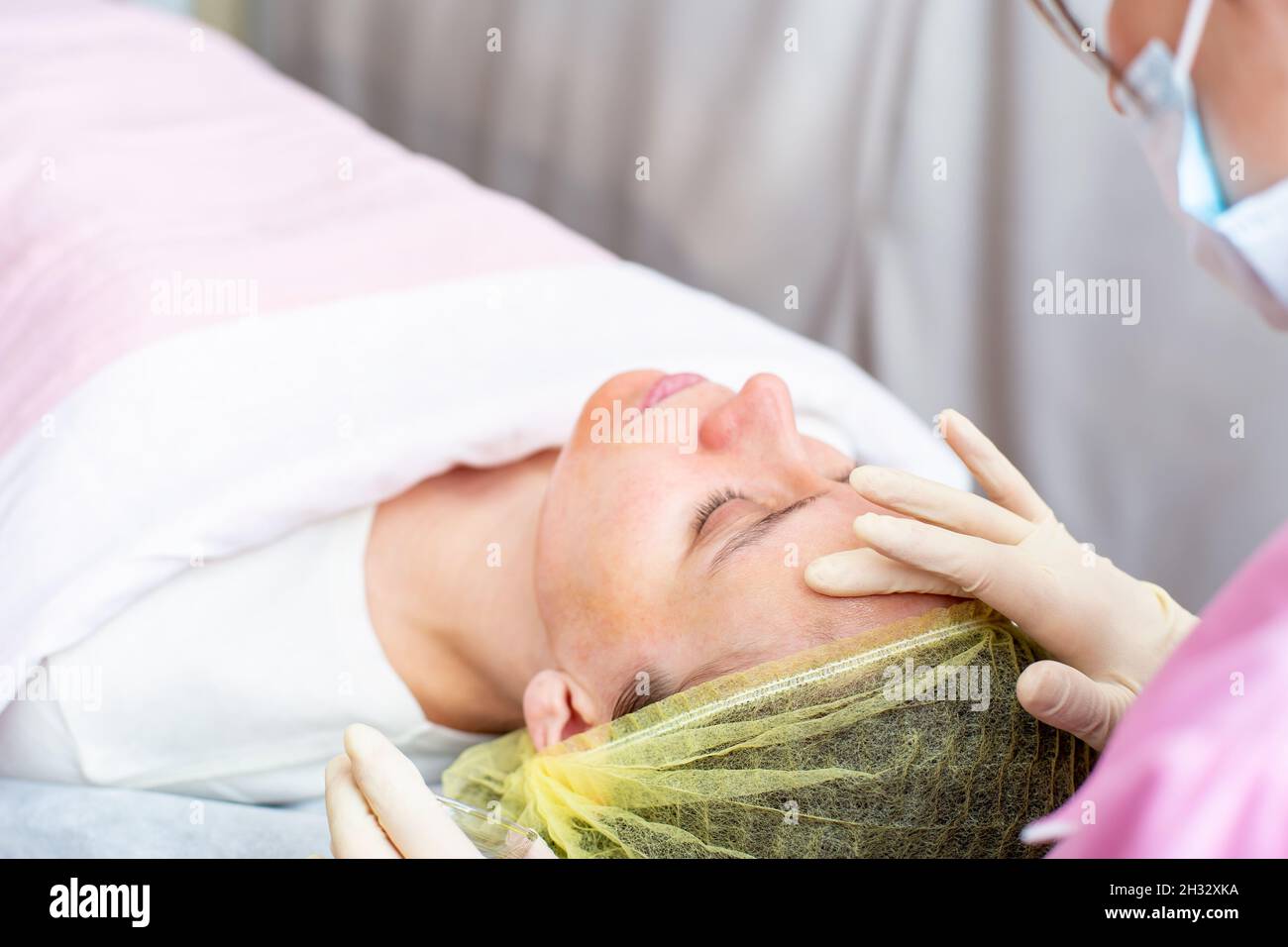 Beautician uses gloved hands to apply a chemical peeling solution to the patient face.  Stock Photo