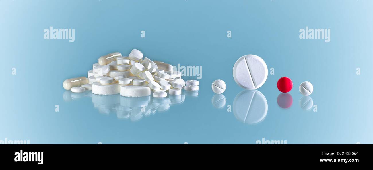 Tablets, pills and capsules. Mountain and roll side by side, many white and one red. Stock Photo