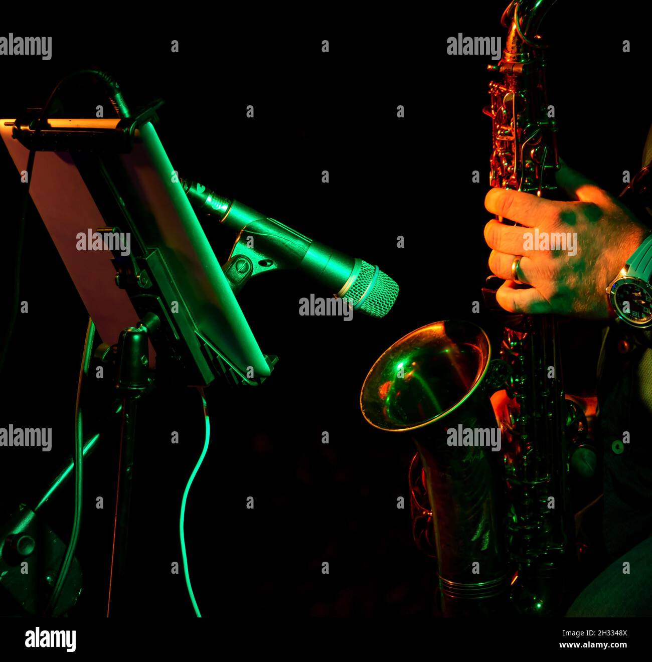 close up hands of artist musician plays the saxophone at a concert in front of the microphone illuminated by orange light Stock Photo