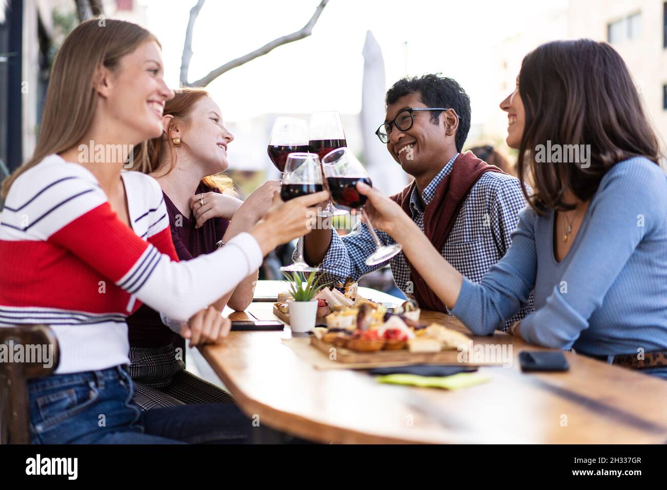 Multiracial friends toasting red wine at the outdoor pub - Food and beverage lifestyle concept with happy people having fun together at pub - Bright f Stock Photo