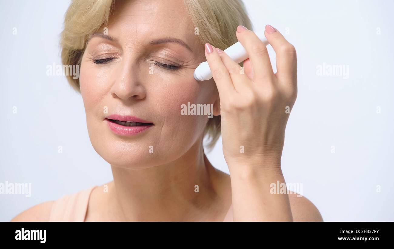 mature woman with closed eyes using eye roller isolated on white Stock Photo