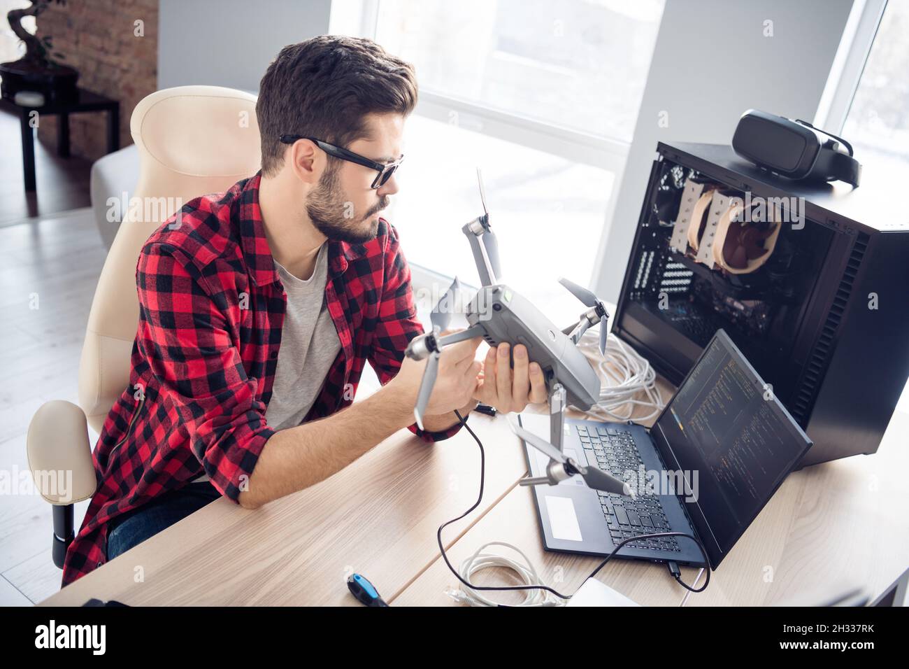 Portrait of attractive clever smart focused guy fixing drone bug software programming code security data at work place station indoors Stock Photo