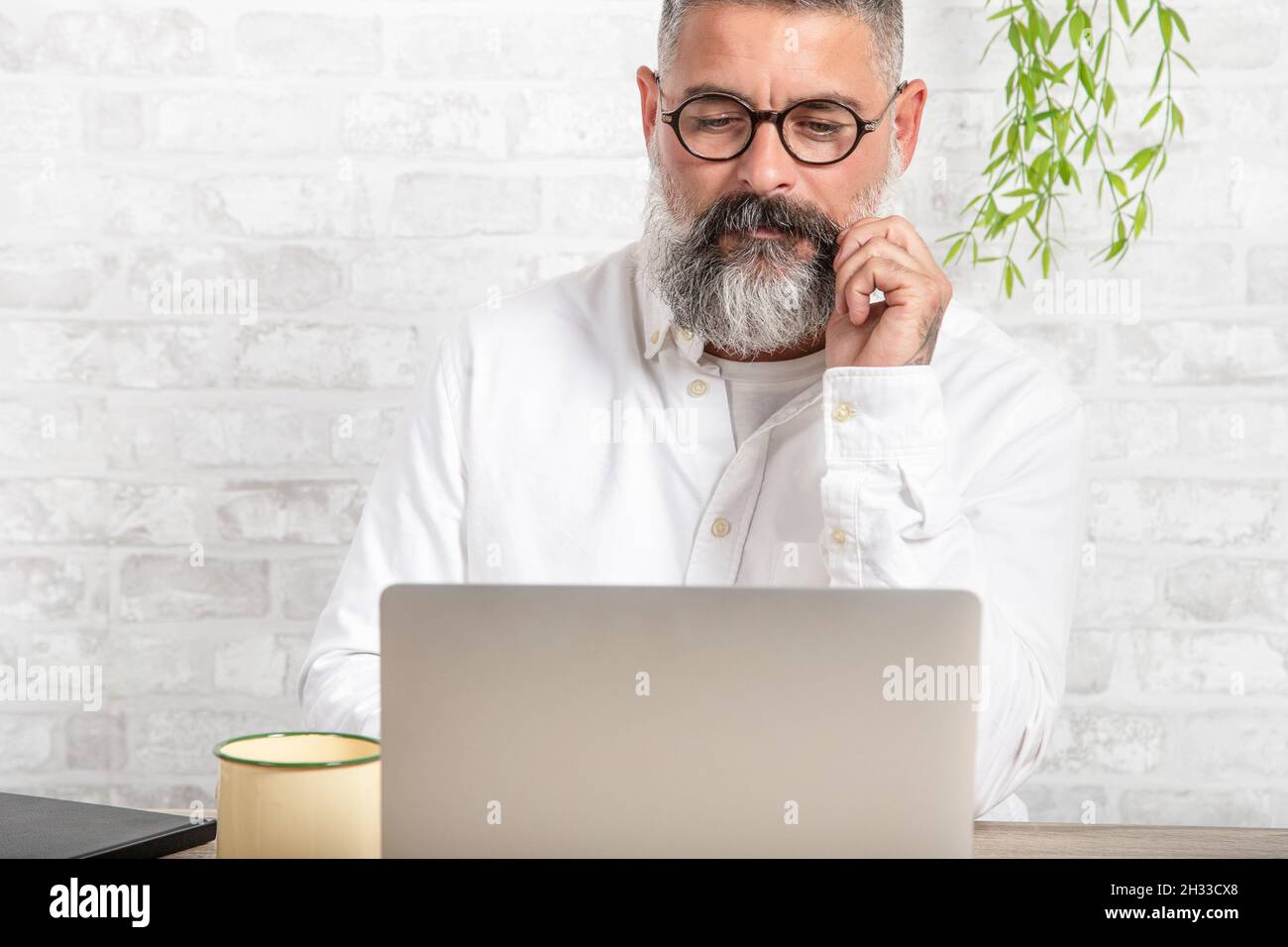 Serious and handsome freelancer sitting in front of computer with thoughtful expression. Stock Photo