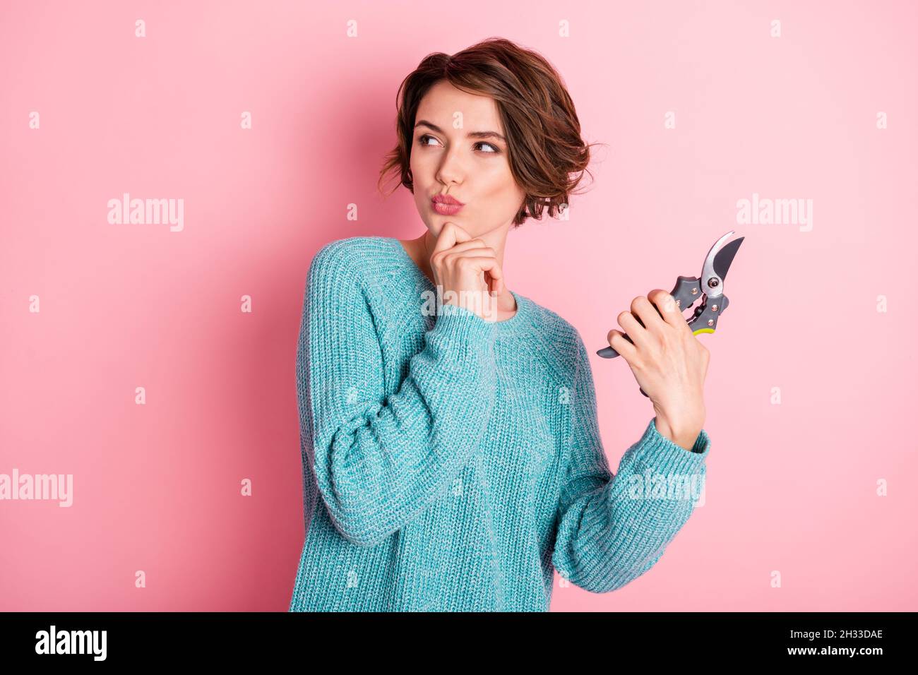 Photo of unsure curly brunette hairdo lady hold tool look empty space wear blue sweater isolated on pink color background Stock Photo