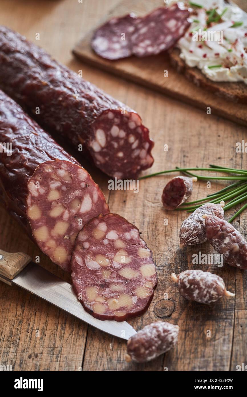 Vertical closeup of dry-cured sausages placed on a wooden table with a knife near a cutting board Stock Photo