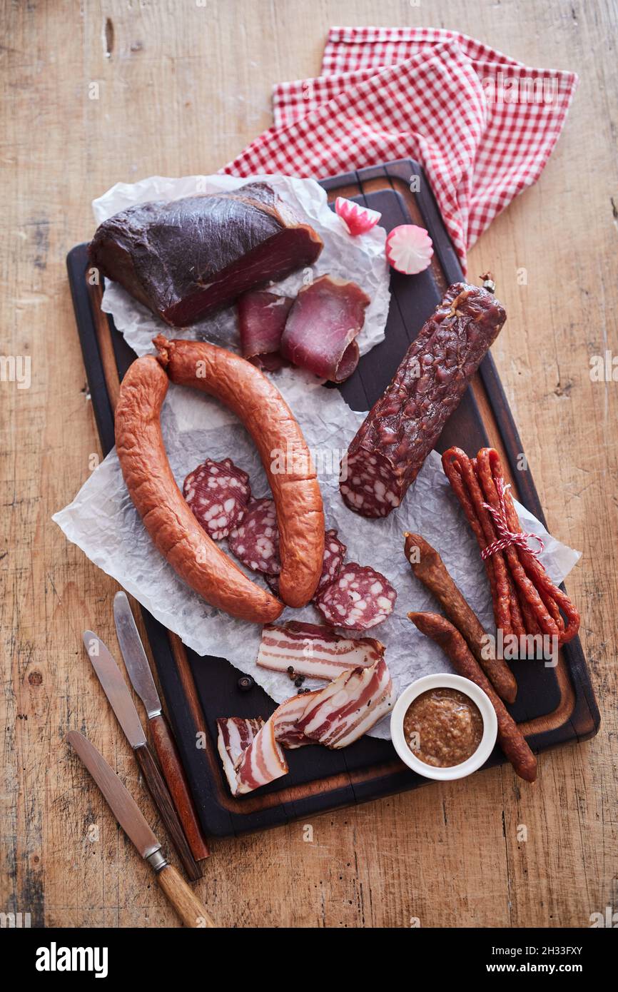 Vertical top view of various cured sausages and smoked lard on a wooden table with knives and napkin Stock Photo