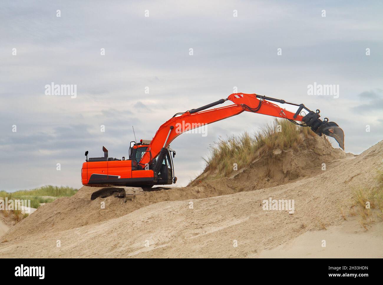 Orange digger working on recovery of dunes after wave attack, the beech of the Dutch island Terschelling Stock Photo