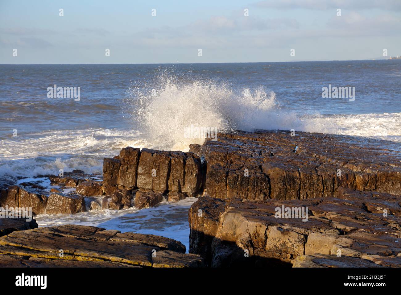 A sunny day with the tide coming in producing fairly small waves splashing into the rocks. Stock Photo