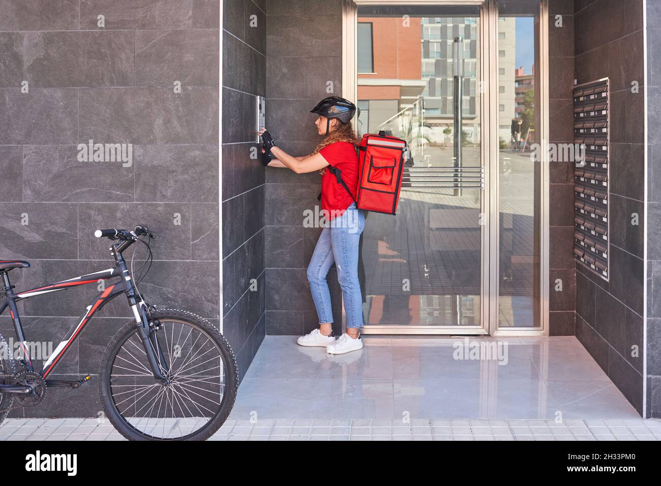A cyclist delivery girl ringing the intercom bell Stock Photo