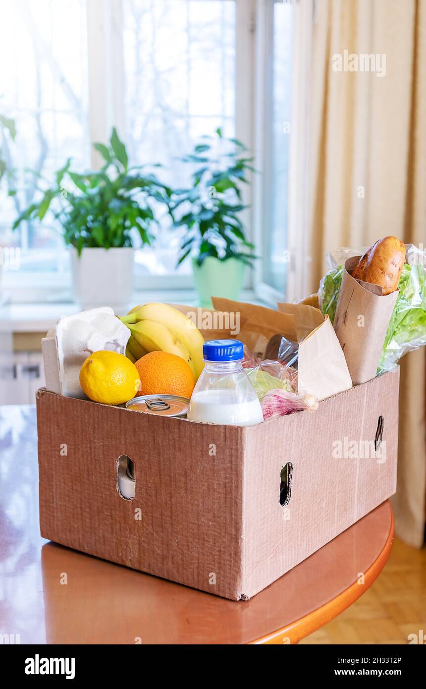 Cardboard box with food products on wooden kitchen table in interior. Safe delivery concept