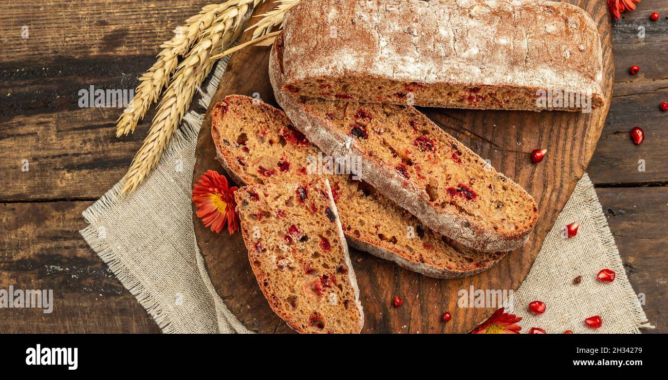 Whole grain bread with cranberry for holidays. Fresh homemade bakery, ripe pomegranate, dry spikelets. Autumn chrysanthemums, vintage wooden backgroun Stock Photo