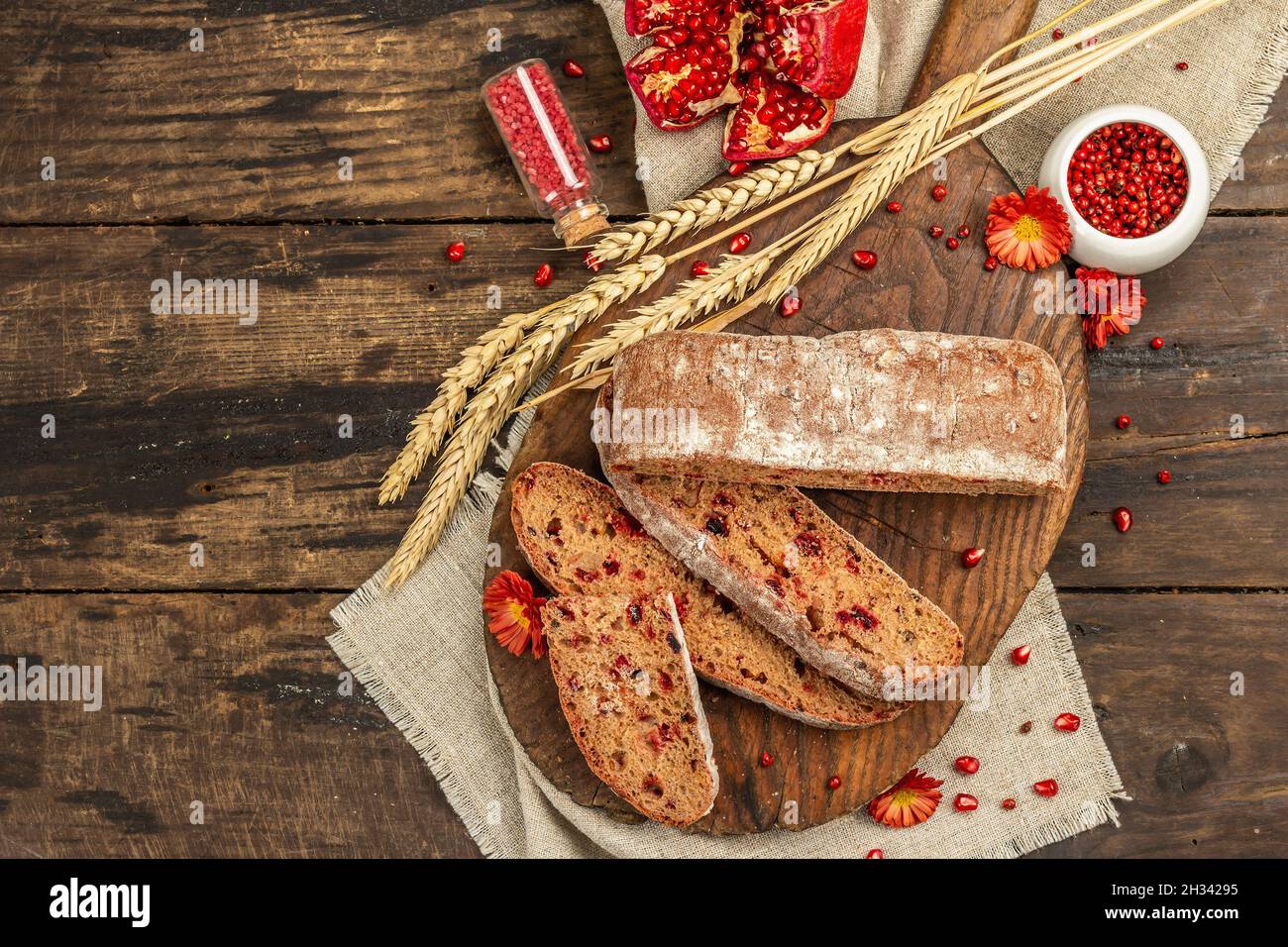 Whole grain bread with cranberry for holidays. Fresh homemade bakery, ripe pomegranate, dry spikelets. Autumn chrysanthemums, vintage wooden backgroun Stock Photo