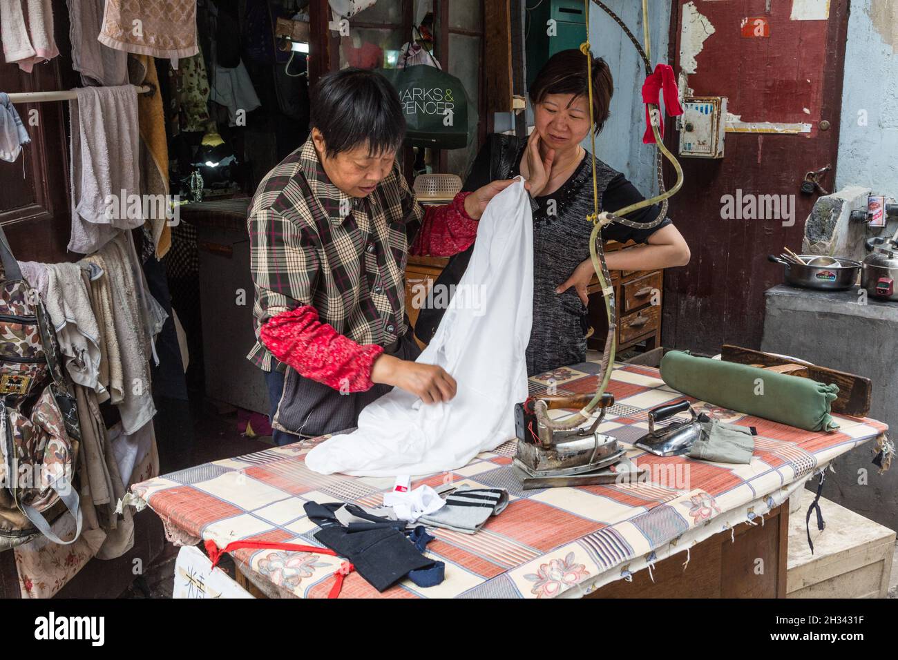 Chinese women ironing clothing in an open streetside tailoring shop in