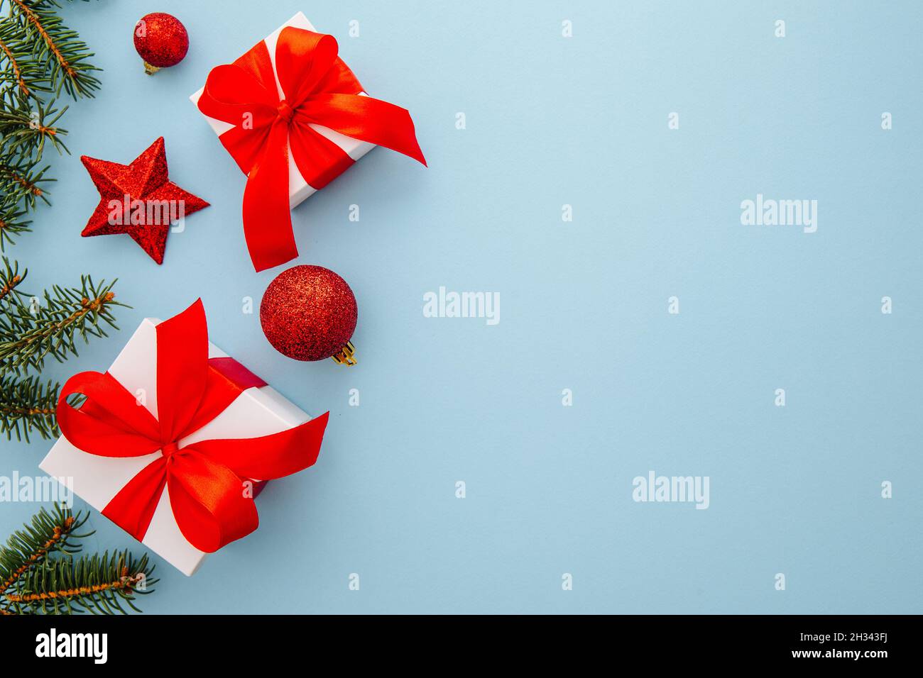 Flat lay with pine tree branches with red christmas balls, stars and gifts on a blue background, christmas, winter, new year concept. Stock Photo
