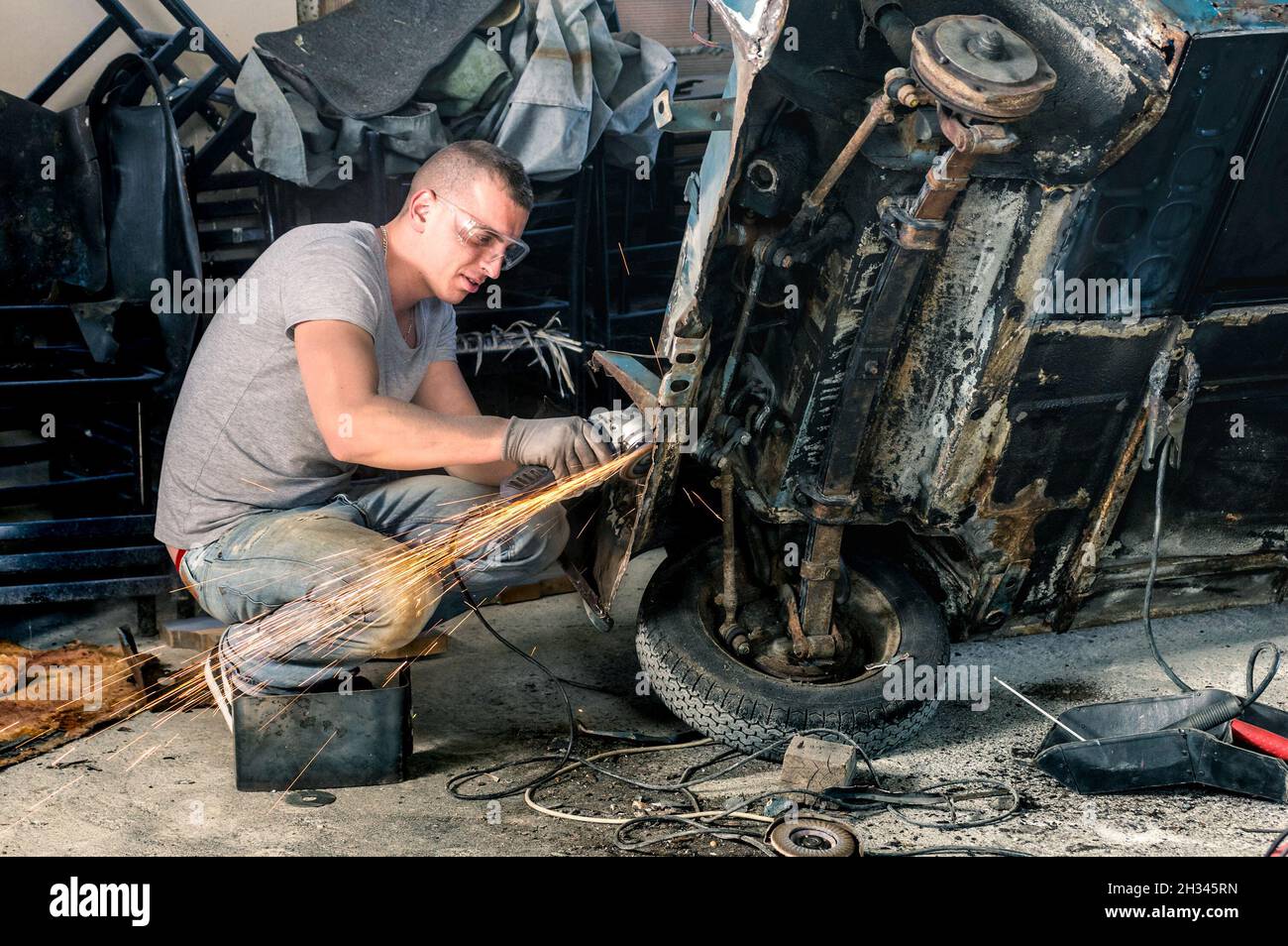 Young mechanical worker repairing an old vintage car body in messy garage Stock Photo