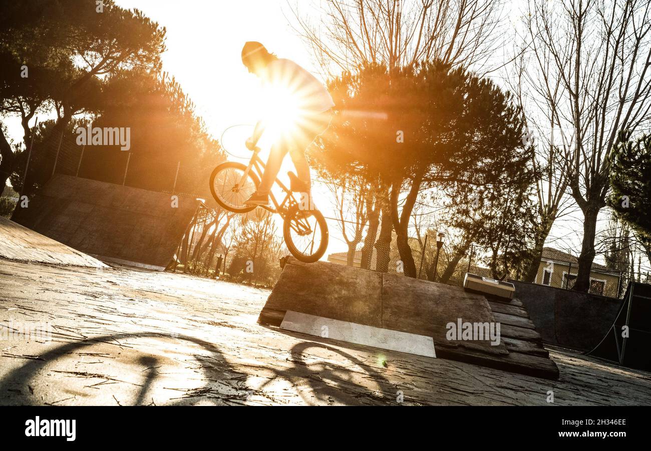 Urban athlete biker performing acrobatic jump at public park - Guy riding bmx bicycle at extreme sport competition on sunny afternoon Stock Photo