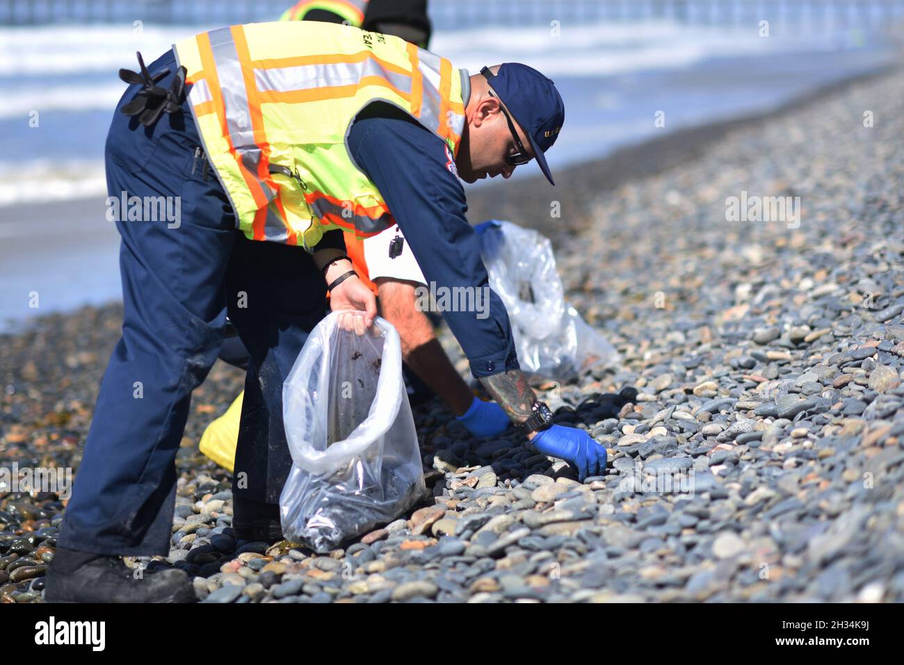 Oceanside Harbor Beach, United States. 12 October, 2021. U.S. Coast Guard PO1 Christopher Romero cleans a tar ball from Oceanside Harbor Beach following an offshore oil spill October 12, 2021 in San Diego County, California. An estimated 144,000 gallons spiked from a pipeline off Huntington Beach on October 1st.  Credit: PO3 Alex Gray/U.S. Coast Guard/Alamy Live News Stock Photo