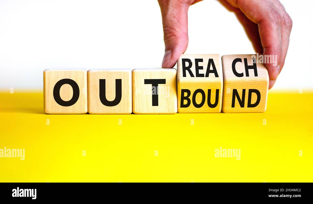 Outreach or outbound symbol. Businessman turns wooden cubes and changes the word 'outbound' to 'outreach'. Beautiful yellow table, white background. B Stock Photo