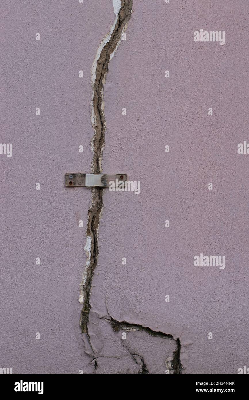 Pale pink cracked wall with survey tell tale wall crack monitor showing the width of the crack gauge surface wall movement Stock Photo