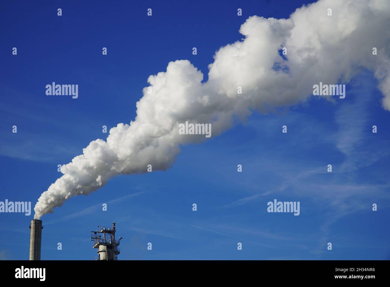 Smoking chimney against bright sun in afternoon makes white clouds up to high sky. Air pollution in bright sun backlight. Environmental pollution. Stock Photo