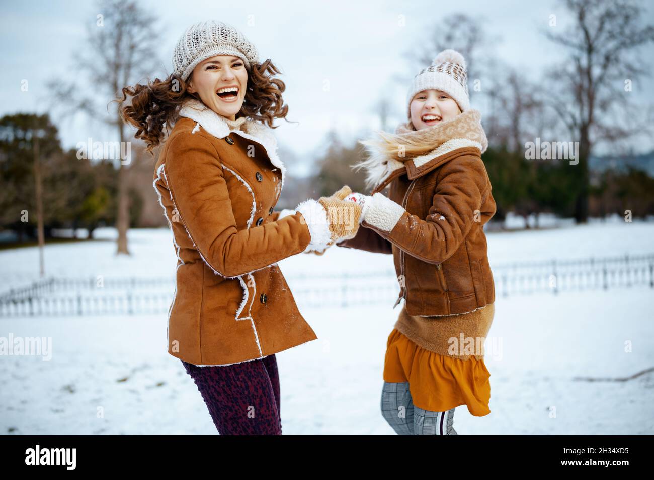 smiling modern mother and child in a knitted hats and sheepskin coats with mittens in a knitted hat and sheepskin coat jumping outdoors in the city pa Stock Photo