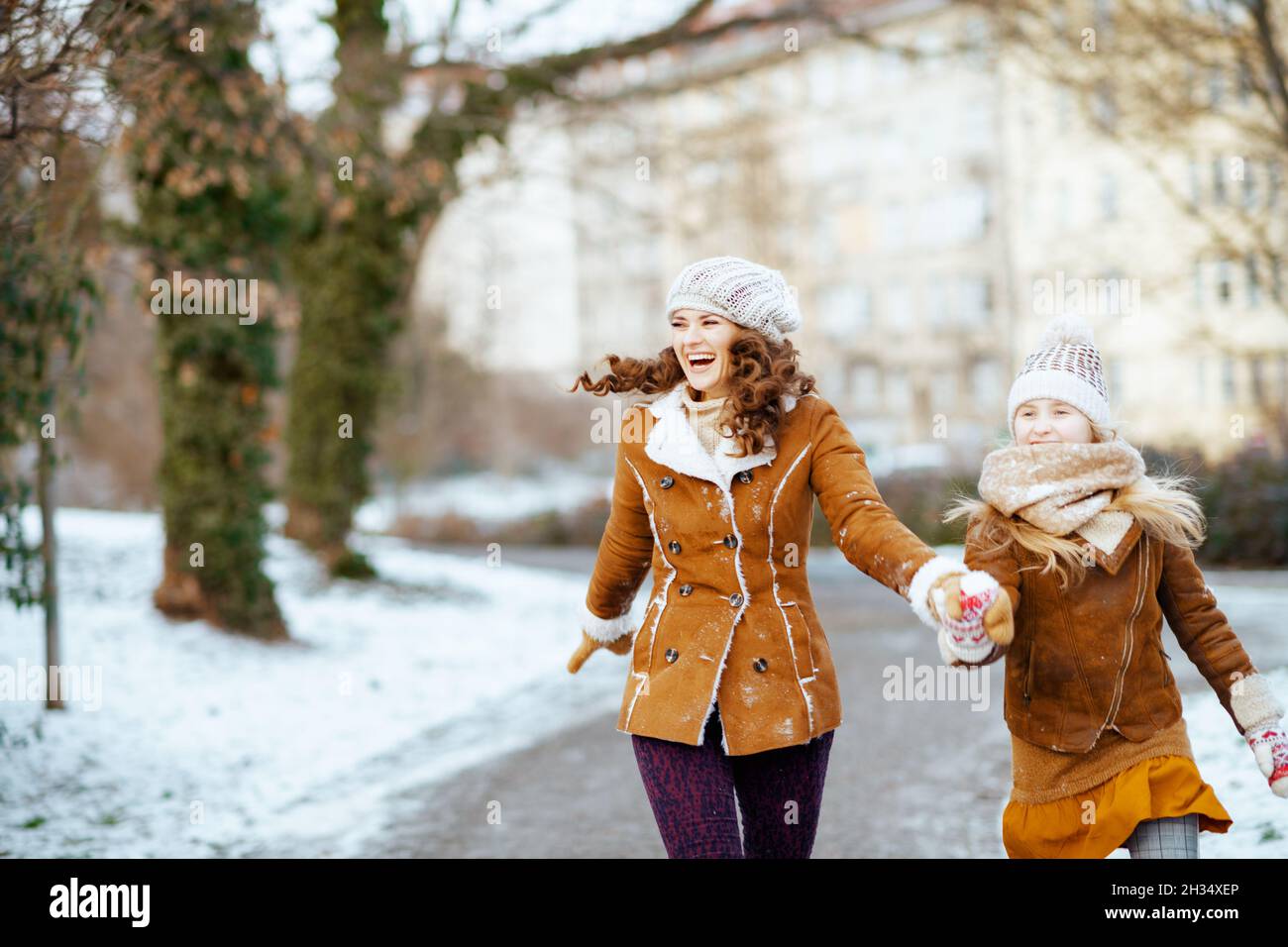 happy elegant mother and child in a knitted hats and sheepskin coats with mittens in a knitted hat and sheepskin coat walking outdoors in the city par Stock Photo