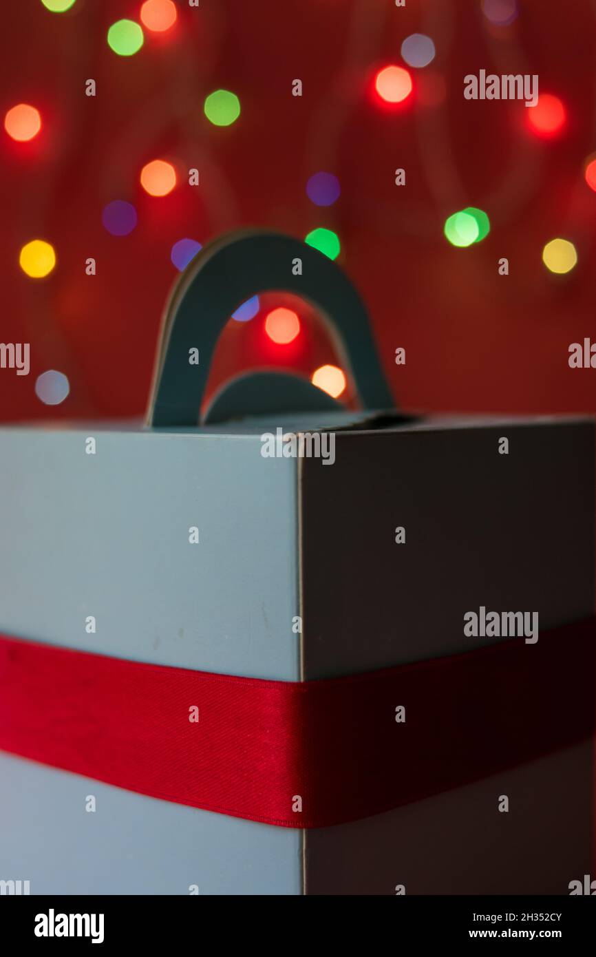 Blue gift box with a red ribbon on a red surface and christmas lights at background Stock Photo
