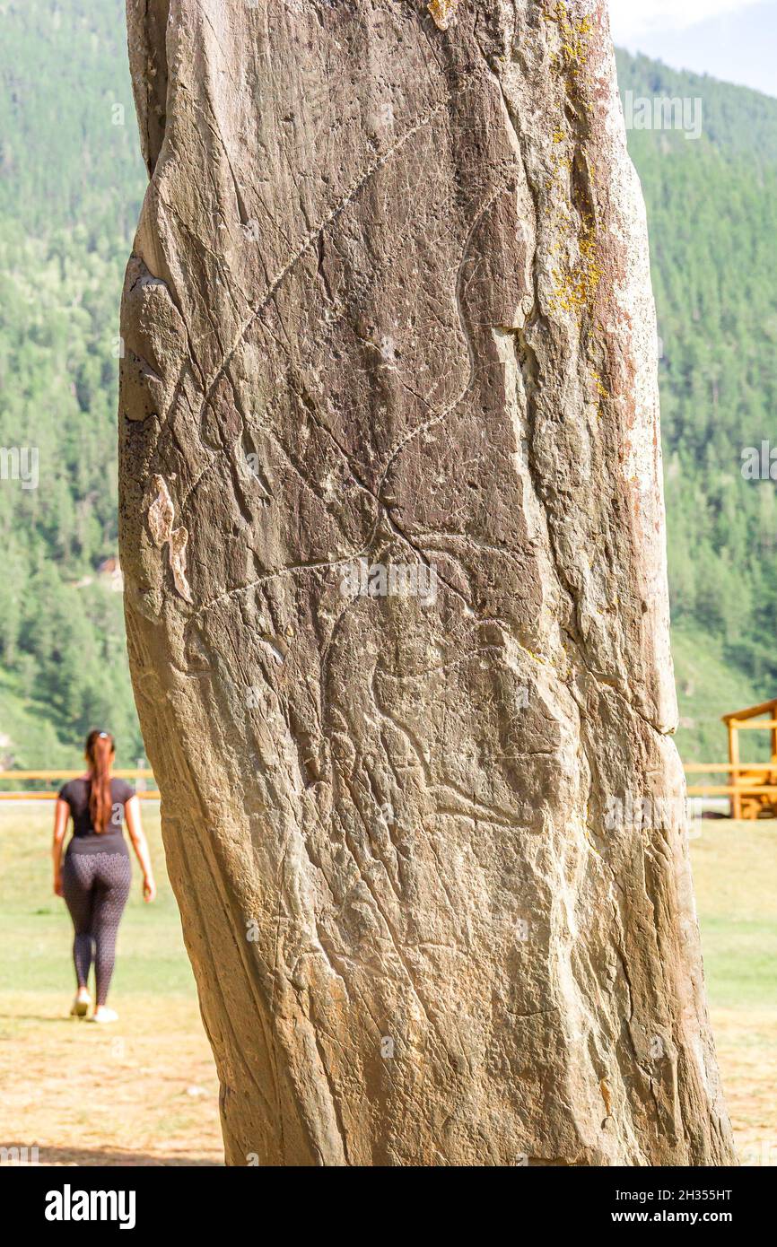 Monument of ancient activity - Deer stone or Olenny stone Adyr-Kan, which is abandoned by young curvy woman. Stone stands by road in free access Stock Photo