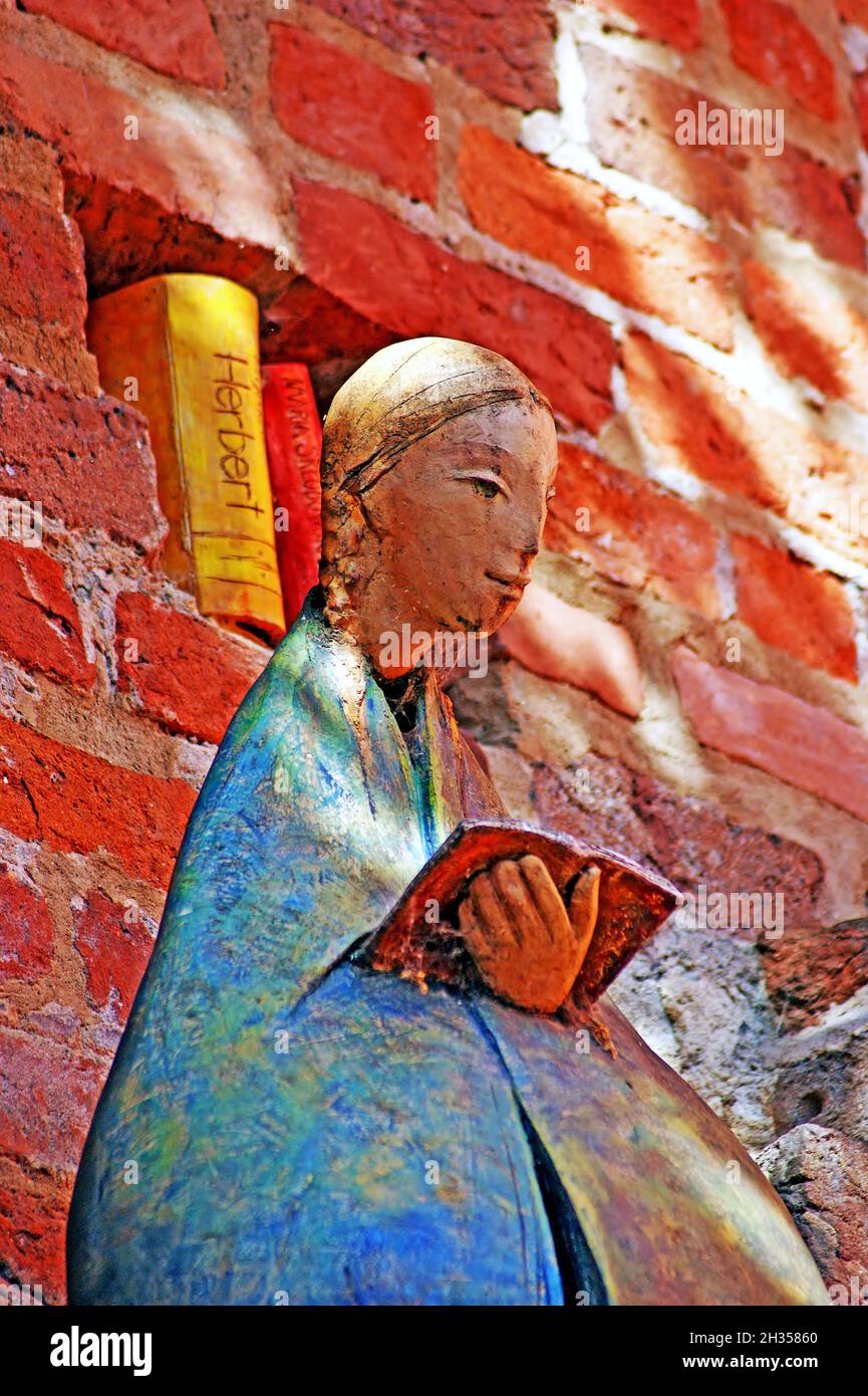 Sculpture of a young blonde female reading a book with books built into the wall behind her in Torun, Poland.  The Gothic brick walls of the old town have become, in parts, a public gallery for outdoor art. Stock Photo