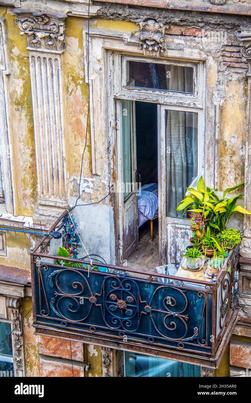 Looking down on a balcony in a grungy deteriorated but beautiful and ornate balcony in Eastern Europe with bed visiable through open doors plants and Stock Photo
