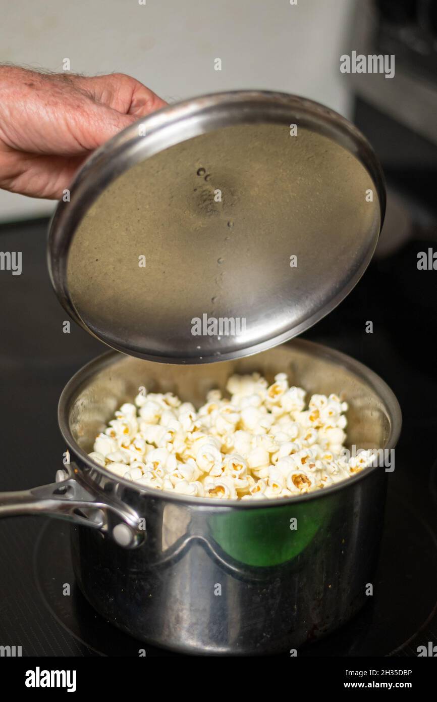 Hand lifts lid of pot revealing hot popcorn Stock Photo Alamy