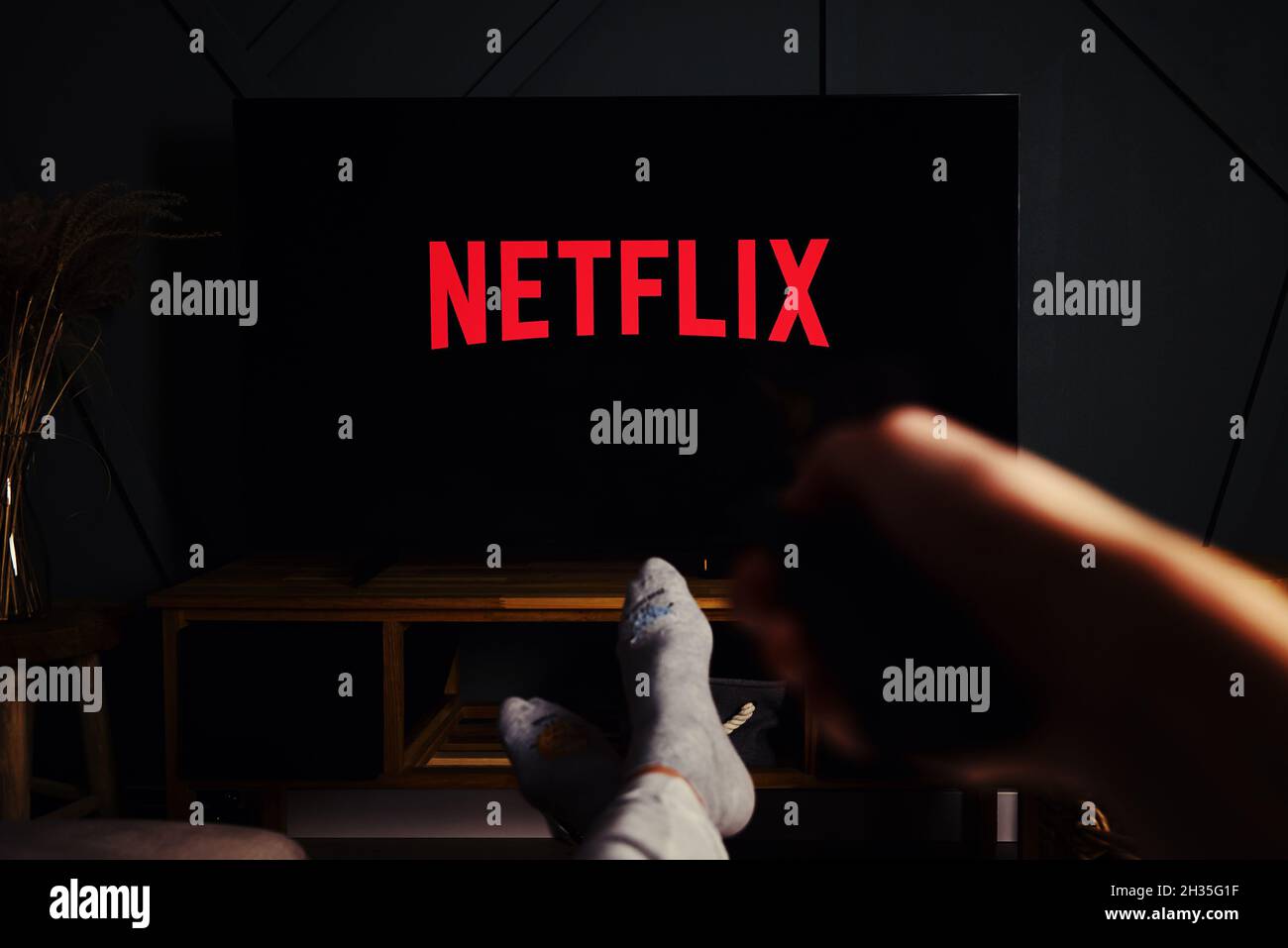 Online streaming service. Boy hold remote control in hand and TV set with NETFLIX service logo. Katy Wroclawskie, Poland - October 25, 2021 Stock Photo