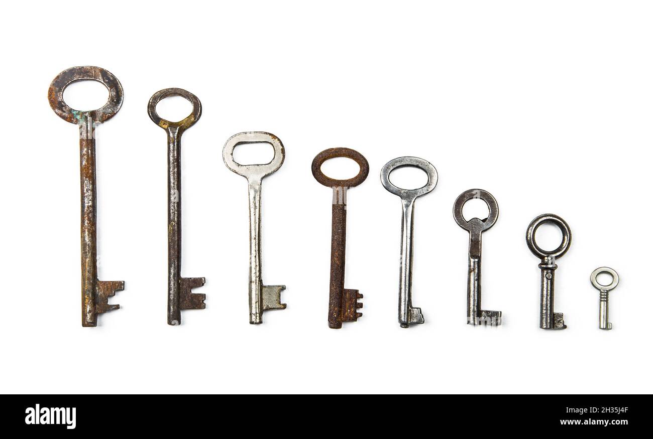Many assorted old multi-colored metal antique keys of different shapes laid out in a row descending from big to small isolated on white background. Ho Stock Photo