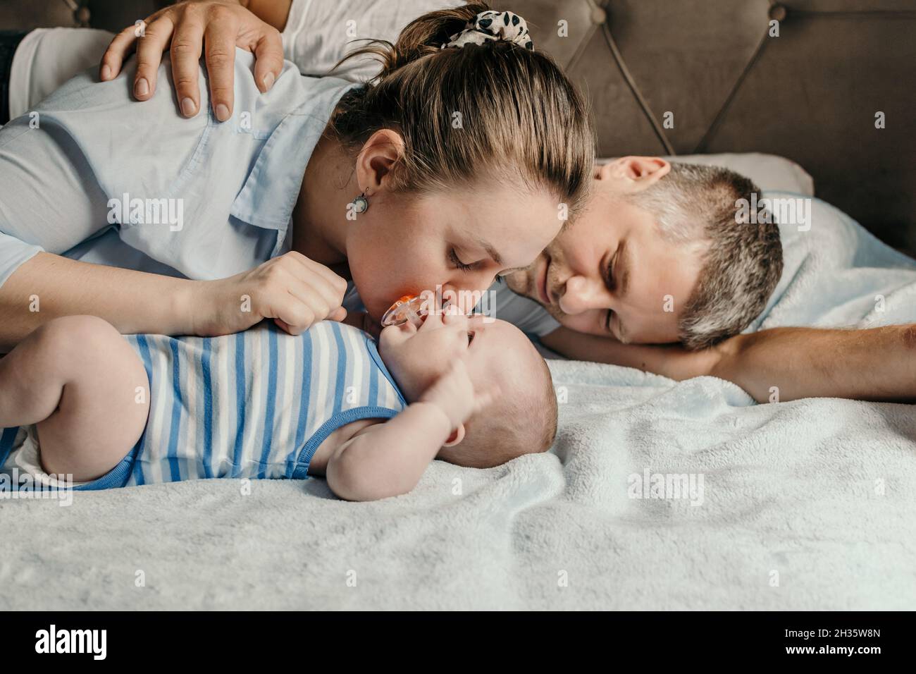 Mother and father cuddling with their newborn baby boy in bed Stock