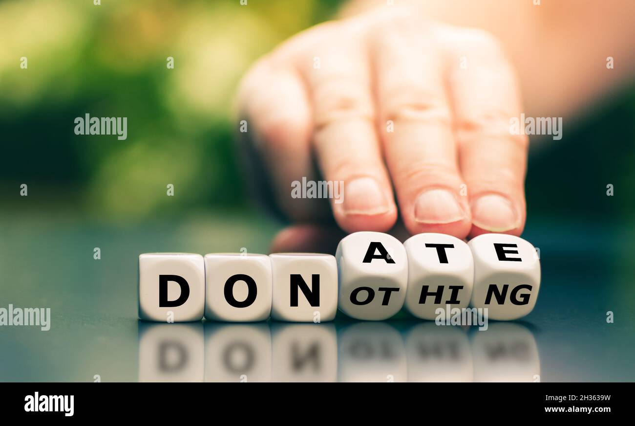Hand turns dice and changes the expression "do nothing" to "donate". Stock Photo