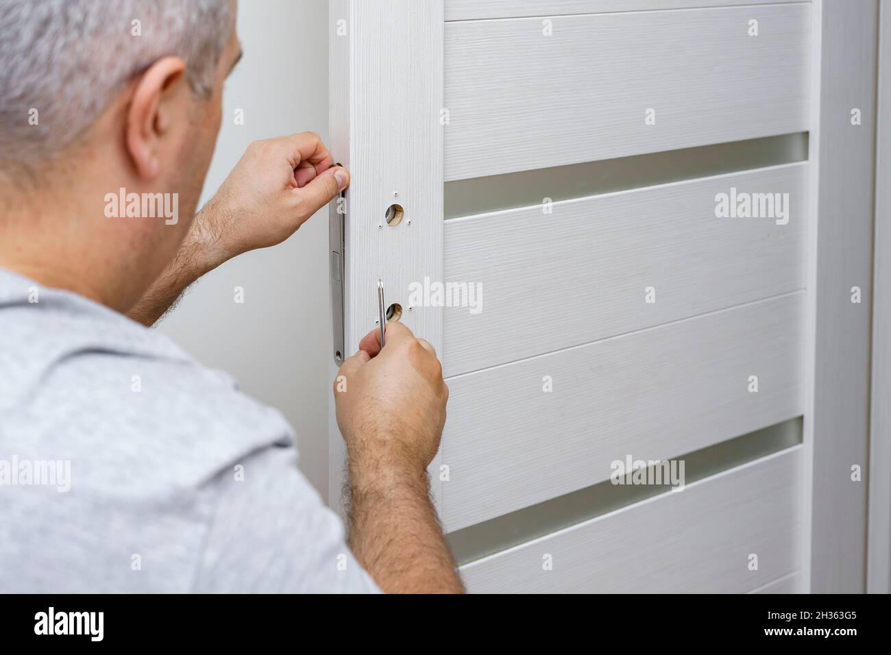 a man fixing a door lock at home using a screwdriver Stock Photo