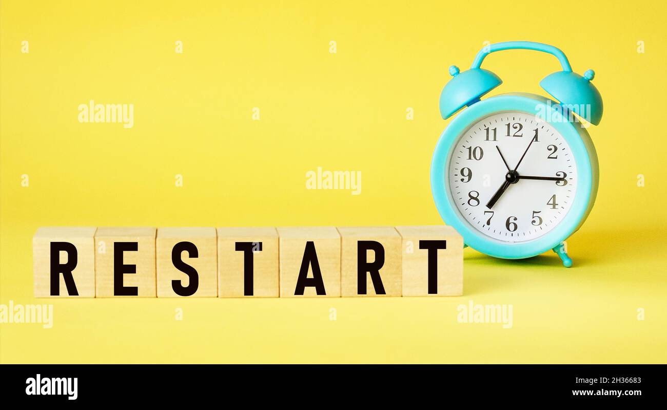 Concept of the word RESTART on cubes on a yellow background with an alarm clock .Business concept. Copy space. Stock Photo