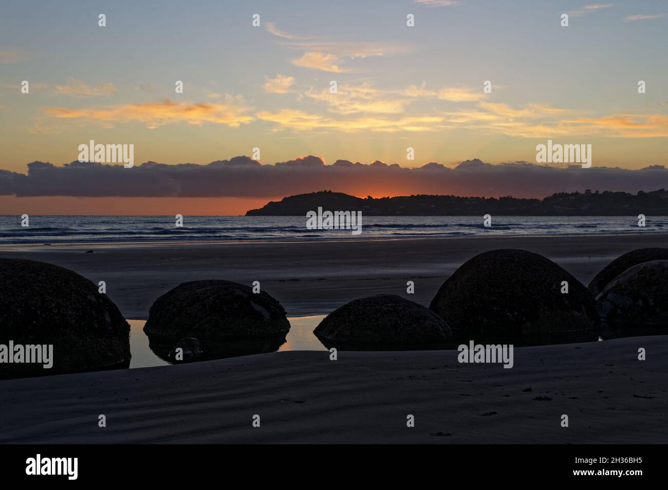 Moeraki Boulders sit in a pool of water on the beach, as the sun comes up, the tide is out. Stock Photo
