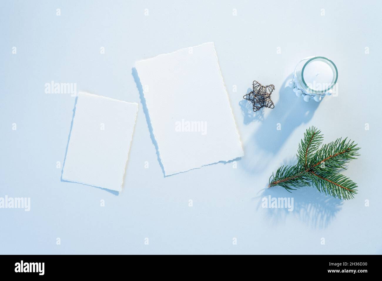Christmas blank greeting card mockup scene. Festive winter wedding composition.Candle, fir tree branch, Christmas decoration on white table.Cold light Stock Photo