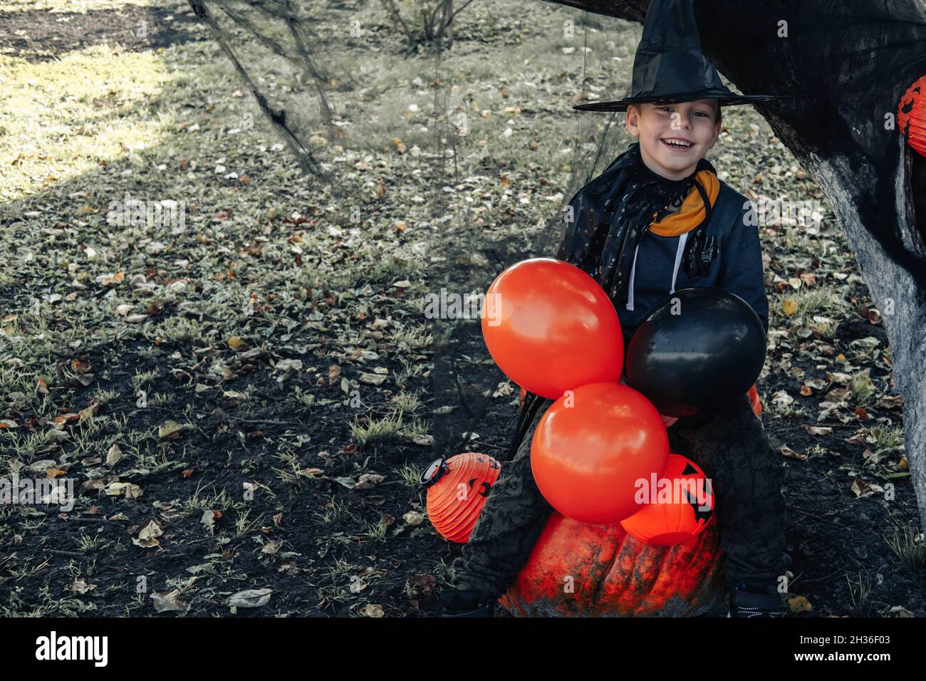 Halloween kids. Cute little boy, child wearing a witch hat with orange and black balloons and a bucket of Jack O Lantern sweets. Happy Halloween. Stock Photo