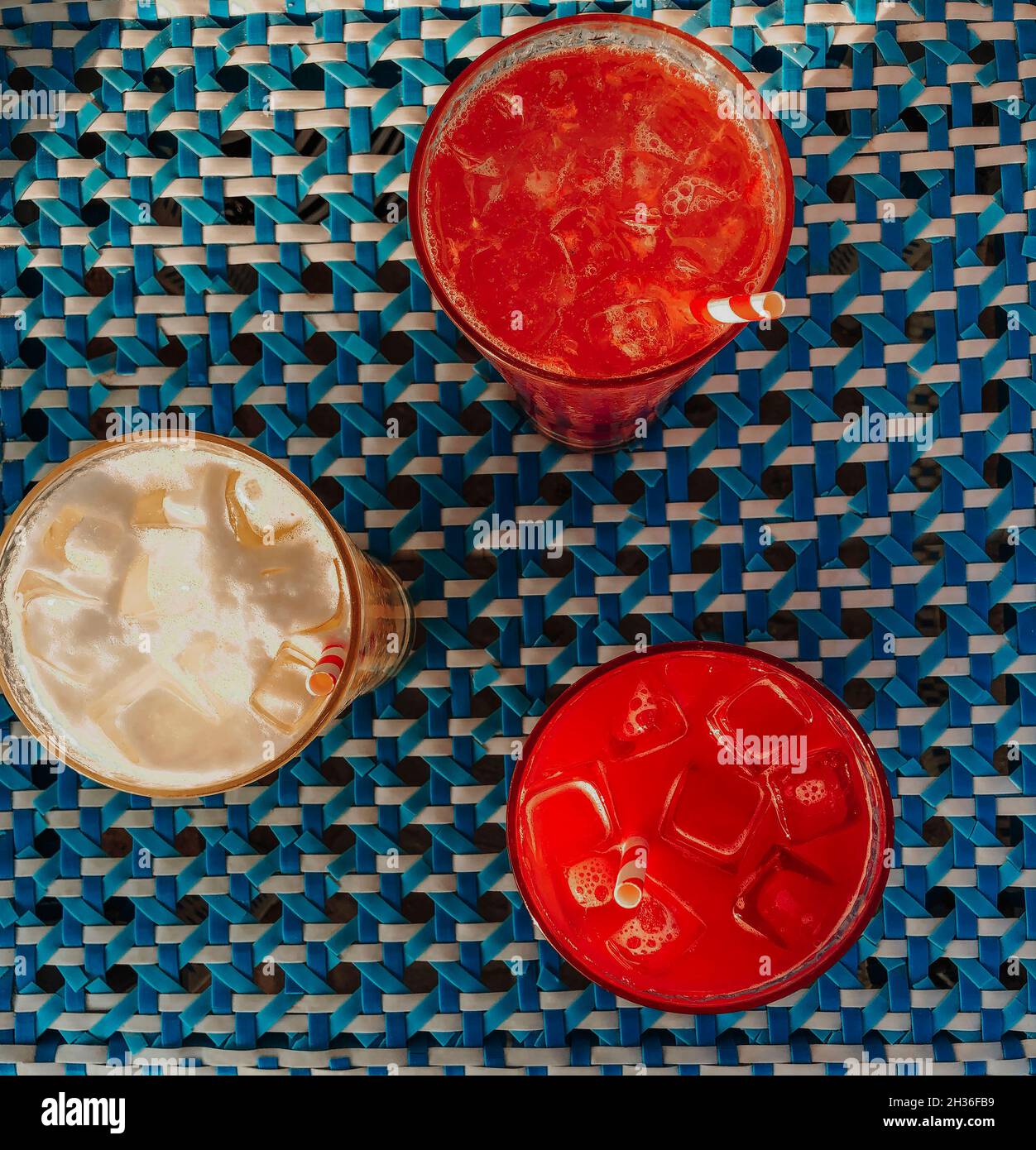 Top view of three different delicious summer cocktails with icecubes on table, glasses with cold refreshing fruit drinks on blue tablecloth Stock Photo