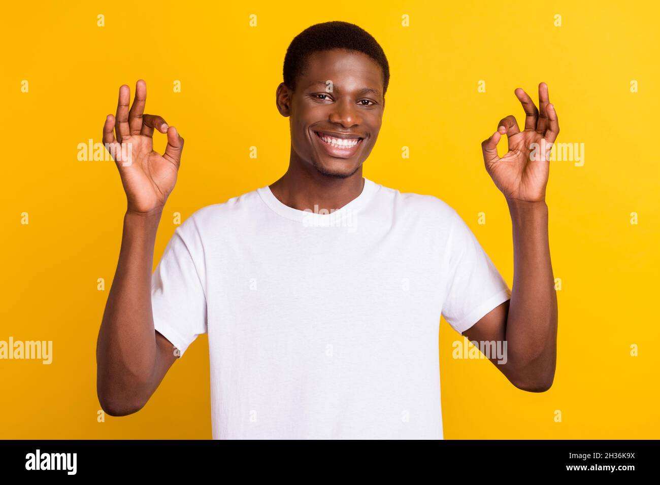 Photo of positive happy dark skin young man hold hands show okay sign ...