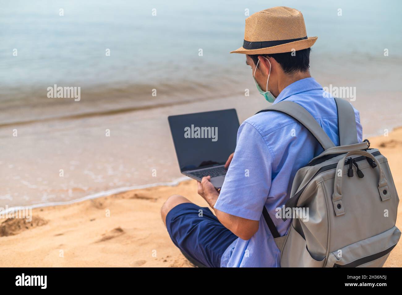 Man wear mask using laptop computer on beach  sea  and Man travel holiday Phuket sandbox Thailand are freedom life financial Stock Photo