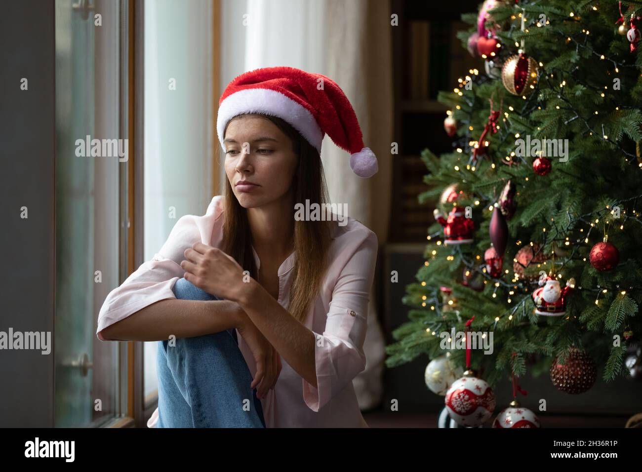 Frustrated Xmas young woman getting bored at Christmas tree Stock Photo