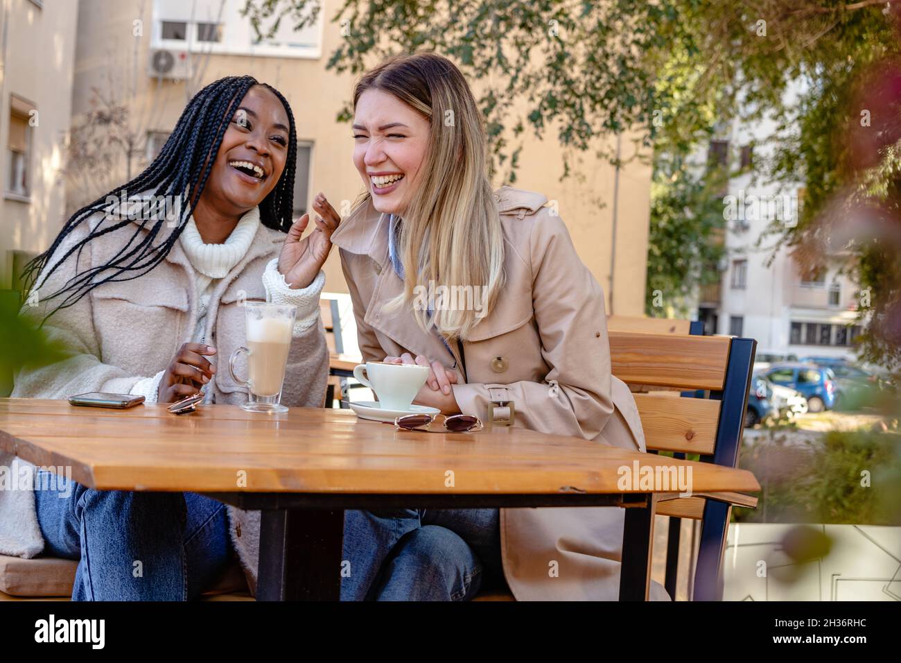 Two young girlfriends enjoying coffee together on a terrace of the