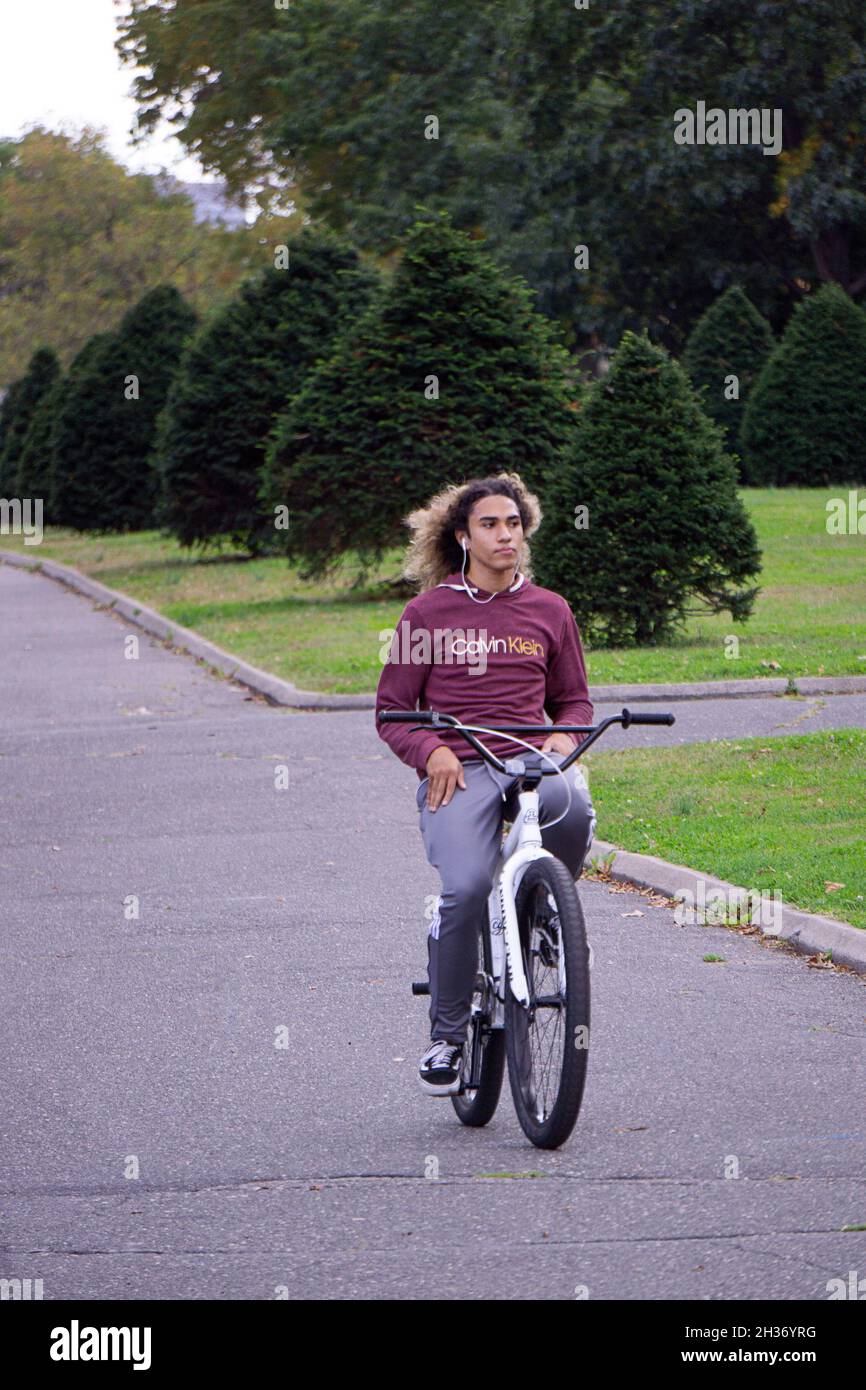 A young man with long hair rides his bikewithout holding onto the handlebars. in Flushing Meadows Corona Park in Queens, New York. Stock Photo