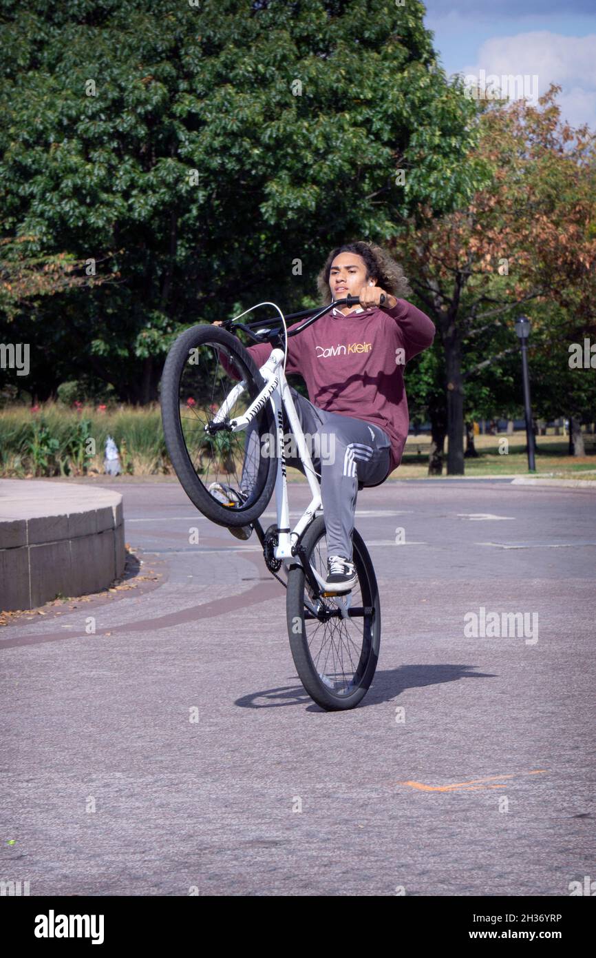 A young man with long hair does wheelies on his bike while riding laps